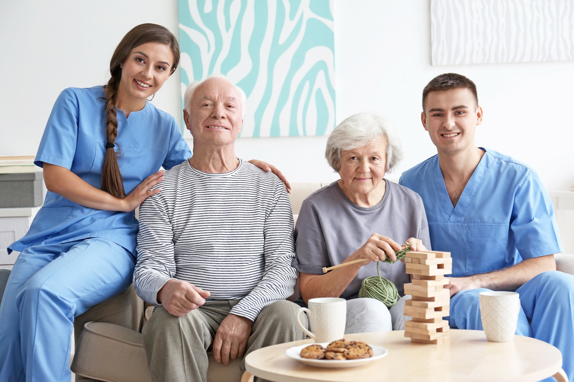 Senior Man and Woman with Young Caregivers Indoors